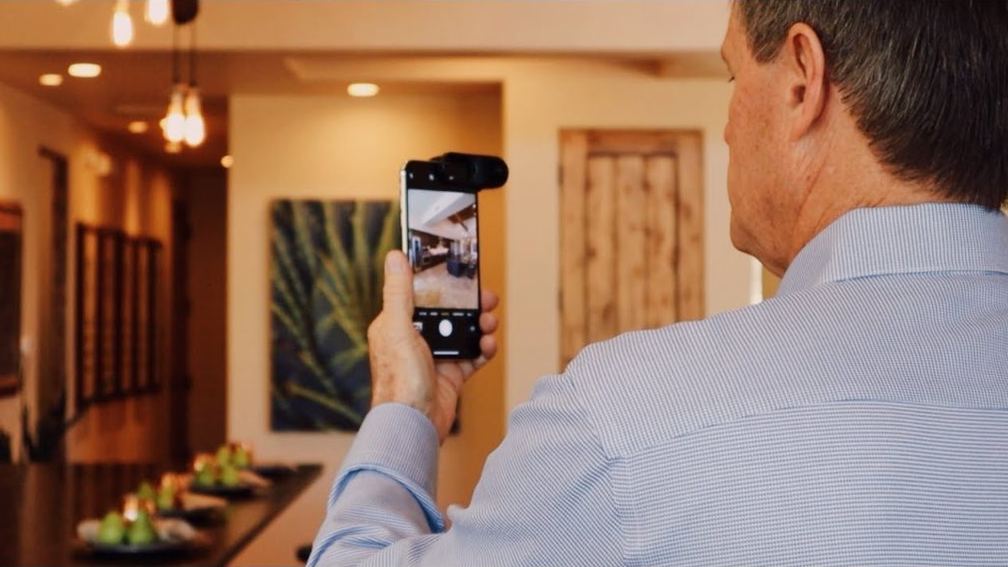 Pessoa fotografando a sala de um imóvel com o celular na mão